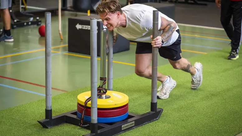 Een deelnemer duwt gewichten voort in een gymzaal.