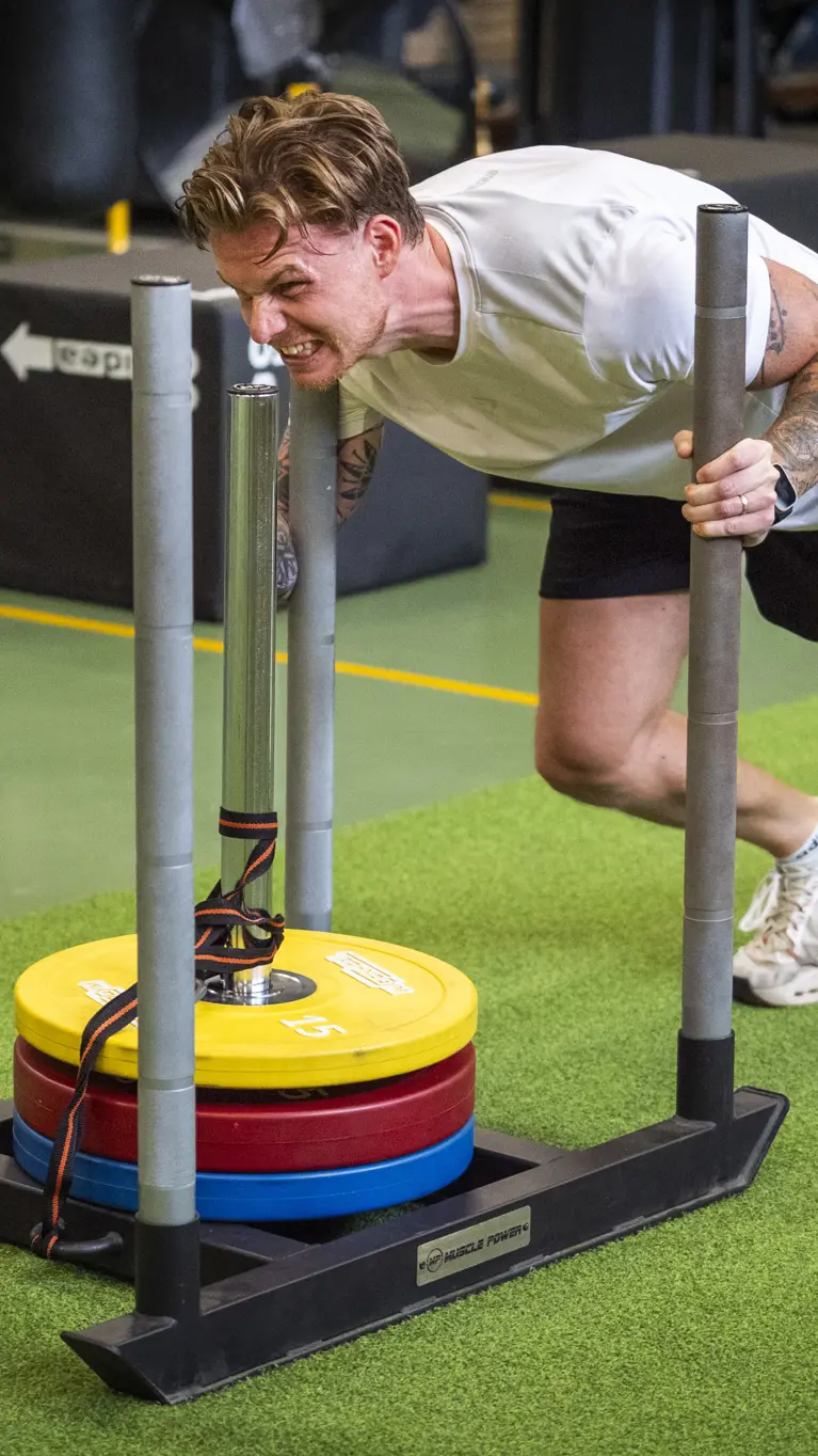 Een deelnemer duwt gewichten voort in een gymzaal.