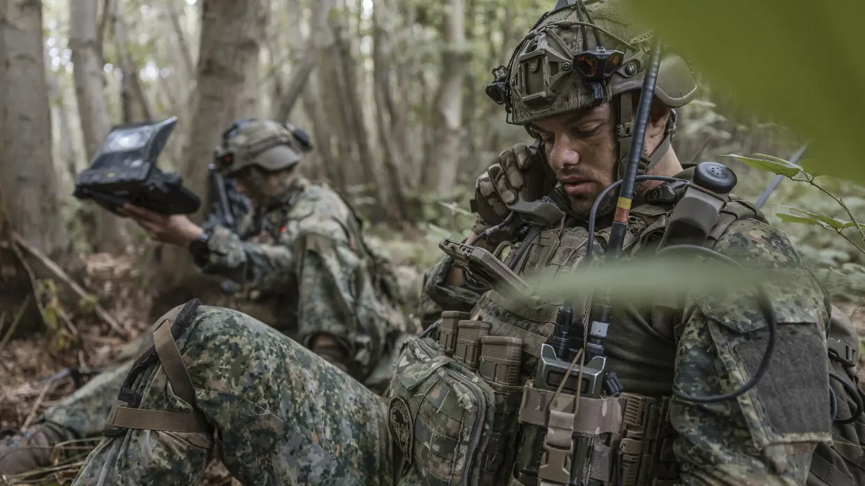 Een militair ligt in het bos en spreekt over de radio.