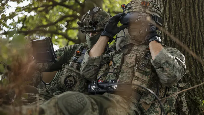 Twee militairen in het bos besturen een drone. 