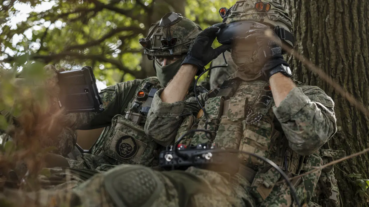 Twee militairen in het bos besturen een drone. 