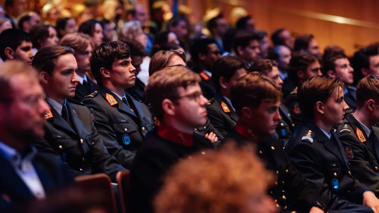 Militairen van verschillende krijgsmachtdelen in hun dagelijks tenue zittend in collegebanken.