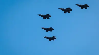 Vijf F-35’s in V-formatie de lucht tegen een strak heldere hemel. 