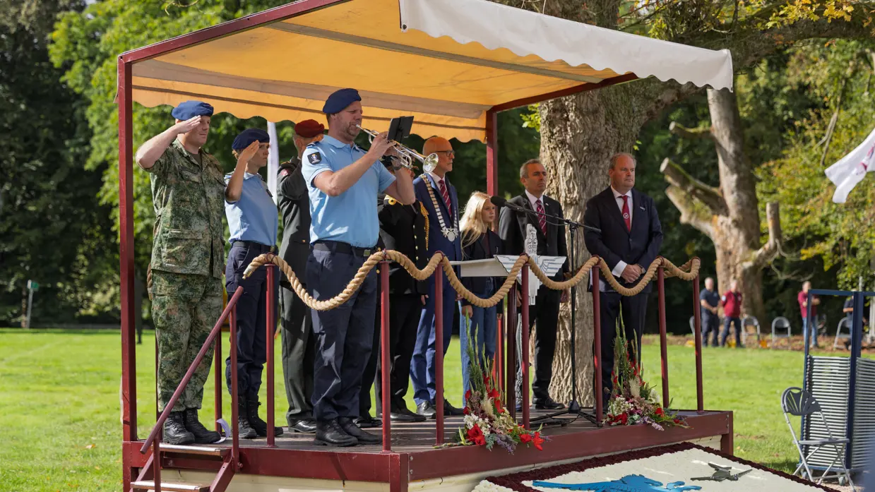 Hoogwaardigheidsbekleders en een trompettist op een podium.