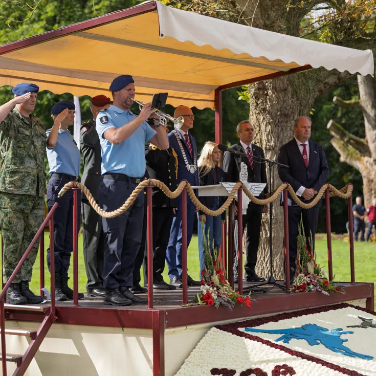 Hoogwaardigheidsbekleders en een trompettist op een podium.