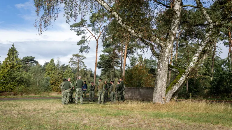 Een groep militairen in overleg met elkaar, staand op een grasveld onder een boom.