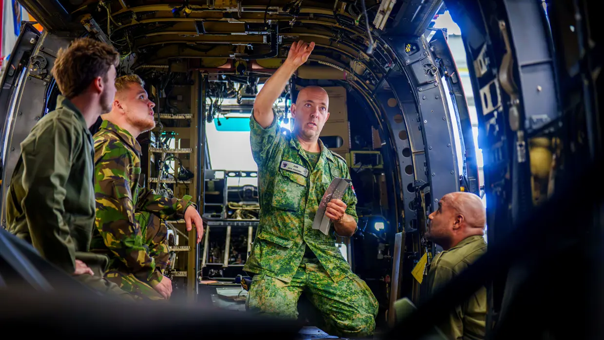 Fotocollage van John Butijn aan het werk als instructeur. Eenmaal heeft hij z’n armen over elkaar en kijkt hij in de camera. Een ander moment helpt hij een leerling bij een aambeeld en zit hij met leerlingen in een gedemonteerde helikopter.