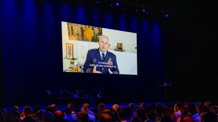 Cds houdt via groot scherm toespraak in zaal met toehoorders.