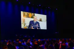 Cds houdt via groot scherm toespraak in zaal met toehoorders.
