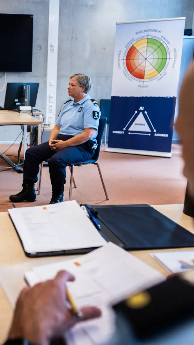Een acteur en marechaussee in gesprek, de instructeur kijkt toe.