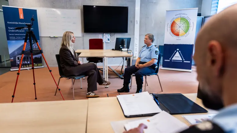 Een acteur en marechaussee in gesprek, de instructeur kijkt toe.