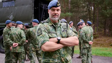 Fotocollage van Ruud. Hij staat voor in de klas en spreekt buiten met leerlingen in een groen gevlekt pak. OP een beeld kijkt hij in de camera met zijn armen over elkaar.  