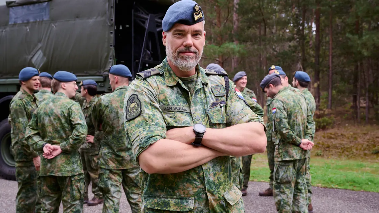 Fotocollage van Ruud. Hij staat voor in de klas en spreekt buiten met leerlingen in een groen gevlekt pak. OP een beeld kijkt hij in de camera met zijn armen over elkaar.  