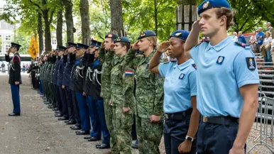 Een lange rij militairen van verschillende krijgsmachtdelen naast elkaar die de eregroet brengen op een plein.