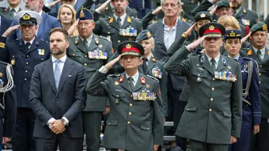 Militairen van verschillende krijgsmachtdelen die de eregroet brengen vanaf een tribune. Vooraan staan Boswijk en Schmidt. Ook staat er een enkele burger tussen.