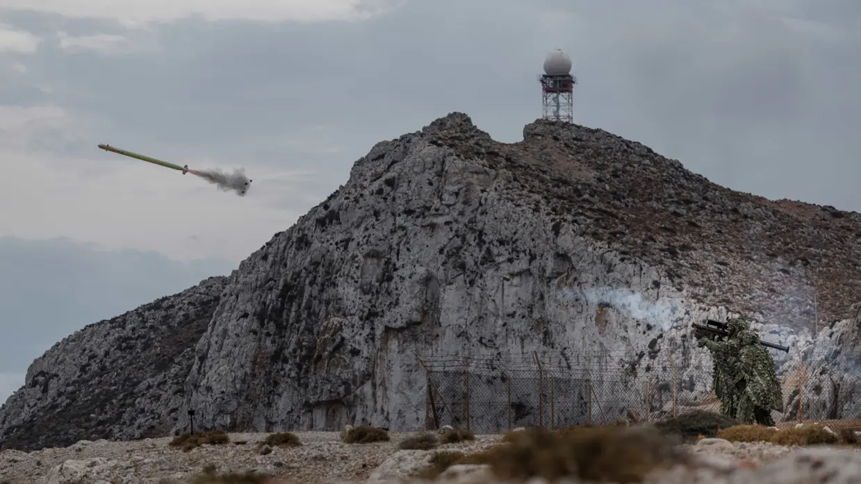 Twee volledig gecamoufleerde militairen schieten een luchtdoelraket af die voorbij de rotsen de lucht in vliegt.