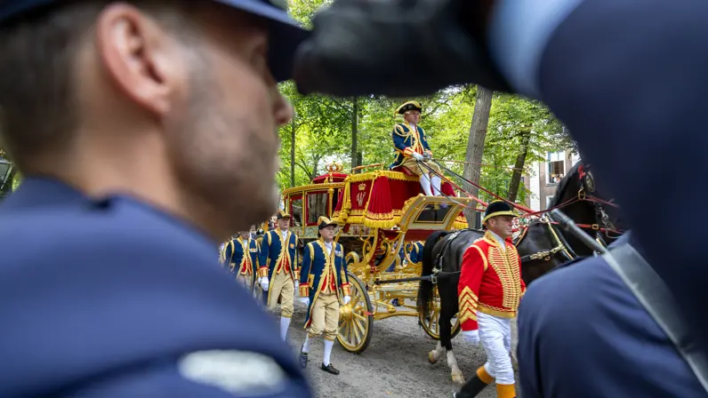 Door de armopening van een luchtmachtmilitair die de eregroet brengt, kijk je op de voorbijrijdende Gouden Koets.
