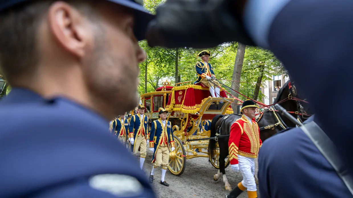 Door de armopening van een luchtmachtmilitair die de eregroet brengt, kijk je op de voorbijrijdende Gouden Koets.