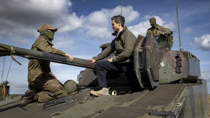 De premier zit naast de loop van een militair voertuig.