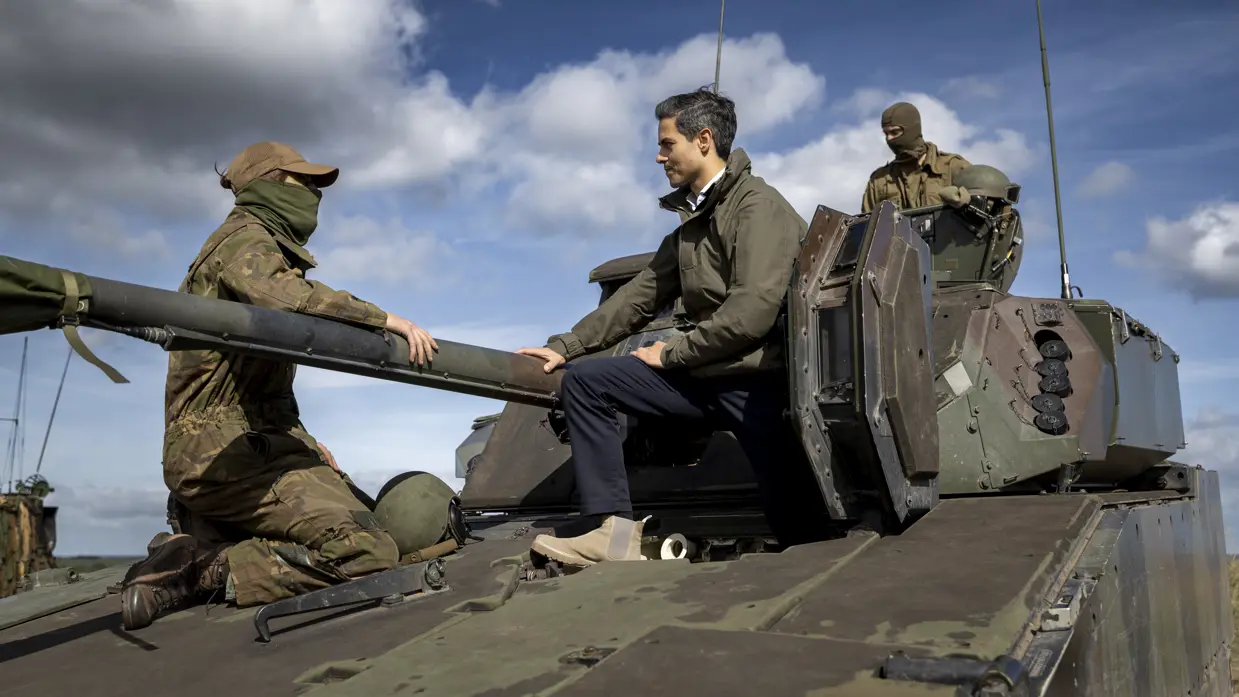 De premier zit naast de loop van een militair voertuig.
