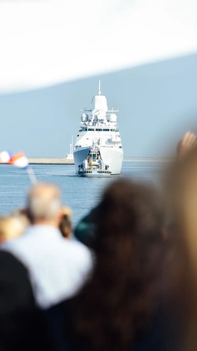  Een marineschip komt aan in de haven terwijl familie aan de kade staat te wachten.