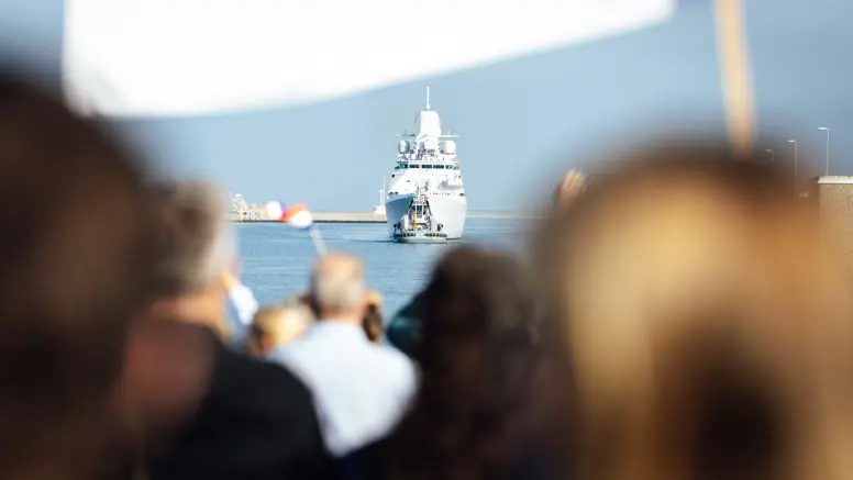  Een marineschip komt aan in de haven terwijl familie aan de kade staat te wachten.
