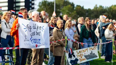 Een grote groep mensen staat aan de kade, enkele van hen houden een spandoek vast.