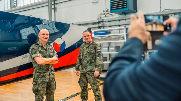 Een blauwe vleugel met rood-witte streep met daarvoor twee militairen die gefotografeerd worden.