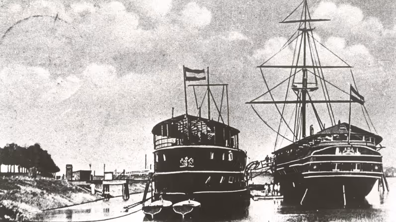 2 historische schepen, een stoomschip en een zeilschip, afgemeerd in een haven bij Gorinchem, met vlaggen en mensen aan boord.