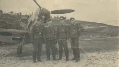 4 mannen staan in uniform voor een vliegtuig met een grote propeller op een open veld met bomen.
