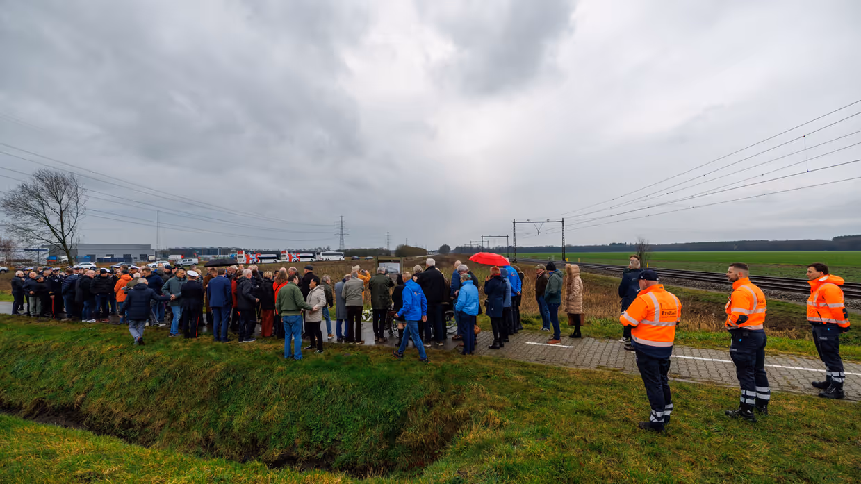Links een groep mensen, waaronder militairen in uniform bij een bord langs de spoorlijn. Rechts: bloemen en kransen bij een bord met daarop een afbeelding van een oude trein, terwijl een moderne trein langs raast.