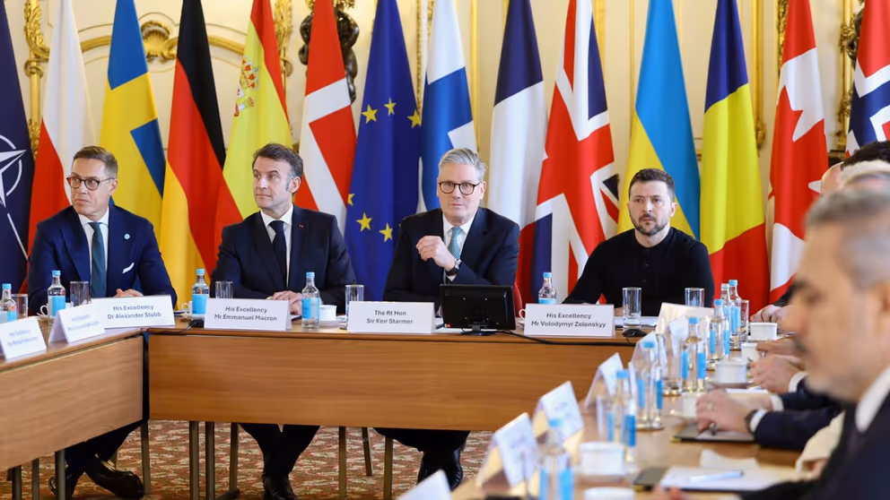 Europese leiders zitten rond een tafel. Vlaggen op de achtergrond.