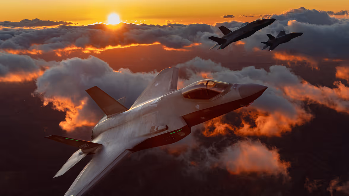 Drie F-35’s boven het wolkendek tegen een oranje lucht met zon.