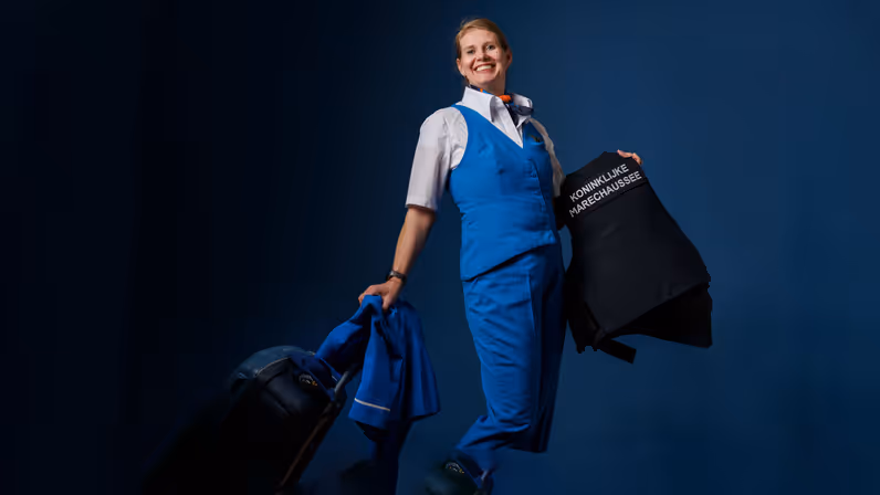 Portret van adjudant Elviera in KLM-pakje en met KMar-jas in de hand.