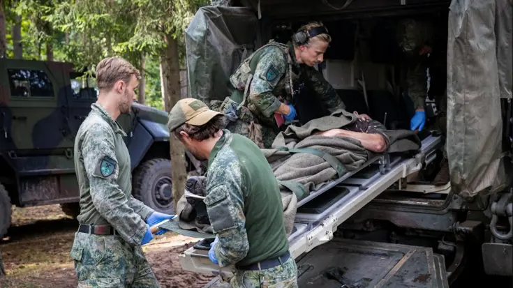3 militairen plaatsen een brancard met een vierde militair in een voertuig