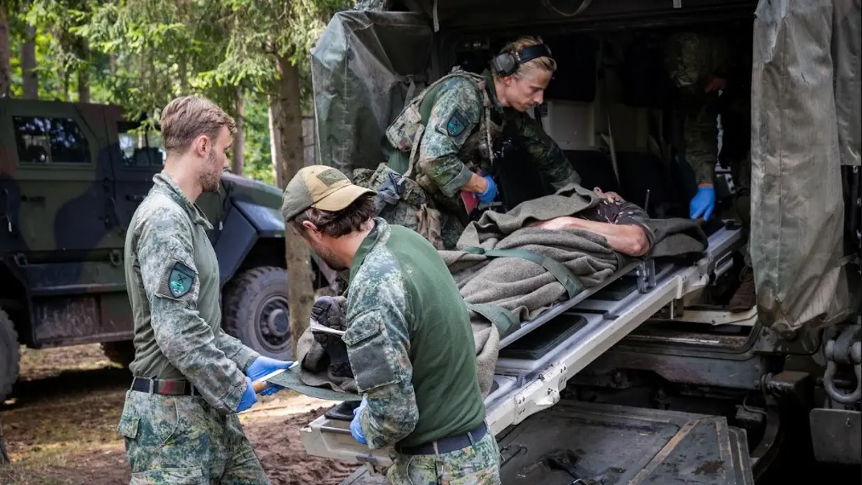 3 militairen plaatsen een brancard met een vierde militair in een voertuig
