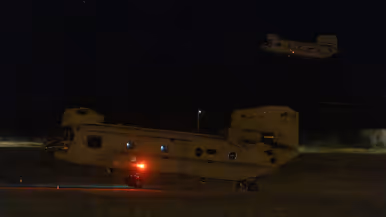 Twee Chinooks in het duister. Een in de lucht, de ander komt net los van het grasveld.