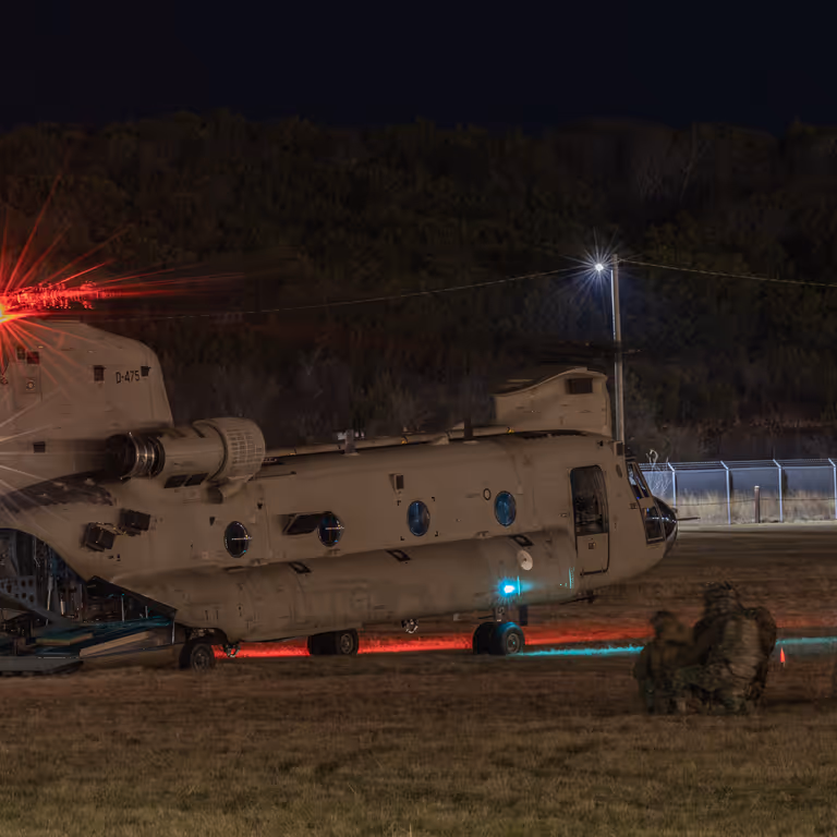 Nachtopname van een Chinook op de grond met luchtmobiele infanteristen er omheen.