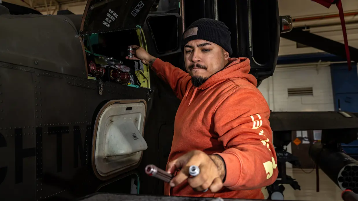 Een Amerikaanse techneut in een oranje trui met capuchon aan het werk aan een Chinook.