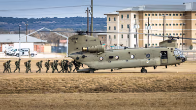 Militairen van 11 Luchtmobiele Brigade lopen via de laadklep een Chinook binnen op een veld van Fort Hood. Op de achtergrond gebouwen en heuvels.