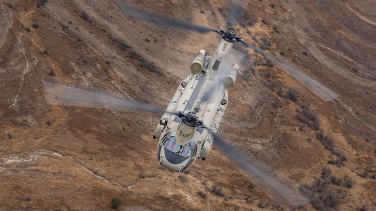 Chinook vliegend boven rood-bruin glooiend landschap.