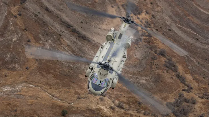 Chinook vliegend boven rood-bruin glooiend landschap.