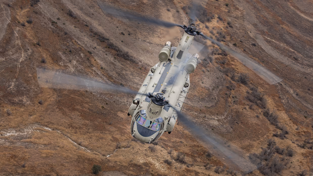 Chinook vliegend boven rood-bruin glooiend landschap.