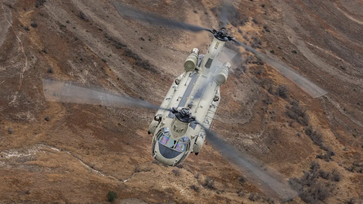 Chinook vliegend boven rood-bruin glooiend landschap.