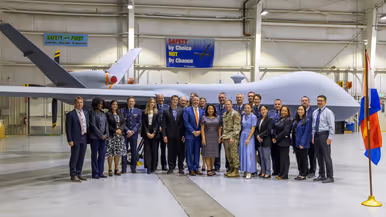 Een groep militairen en burgers poserend voor een MQ-9A Reaper in een hangaar.