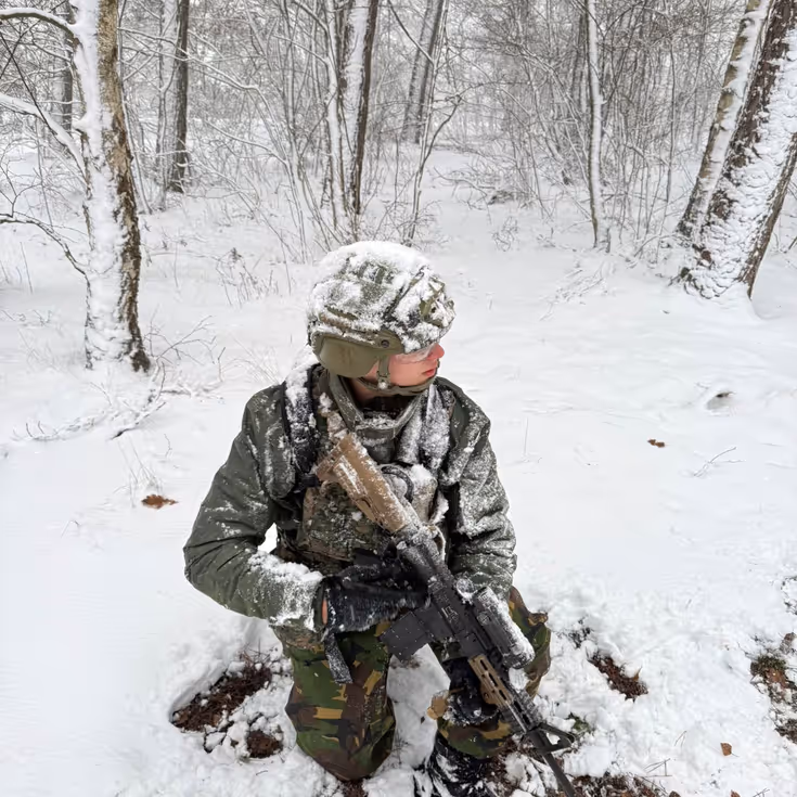 Marechaussee met lang wapen in de sneeuw.