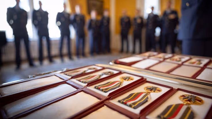 Medailles in doosjes met op de achtergrond onscherp militairen in dagelijks tenue. 