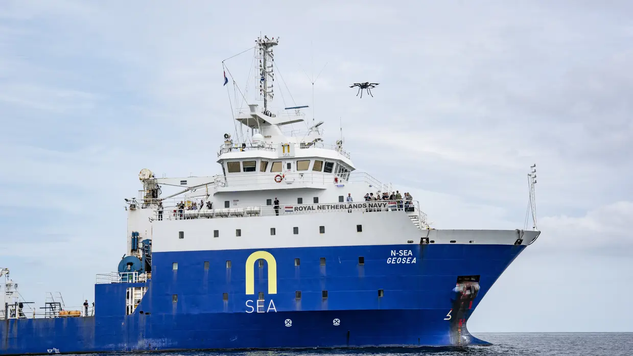 Een drone vliegt boven een groot, blauw schip op zee.