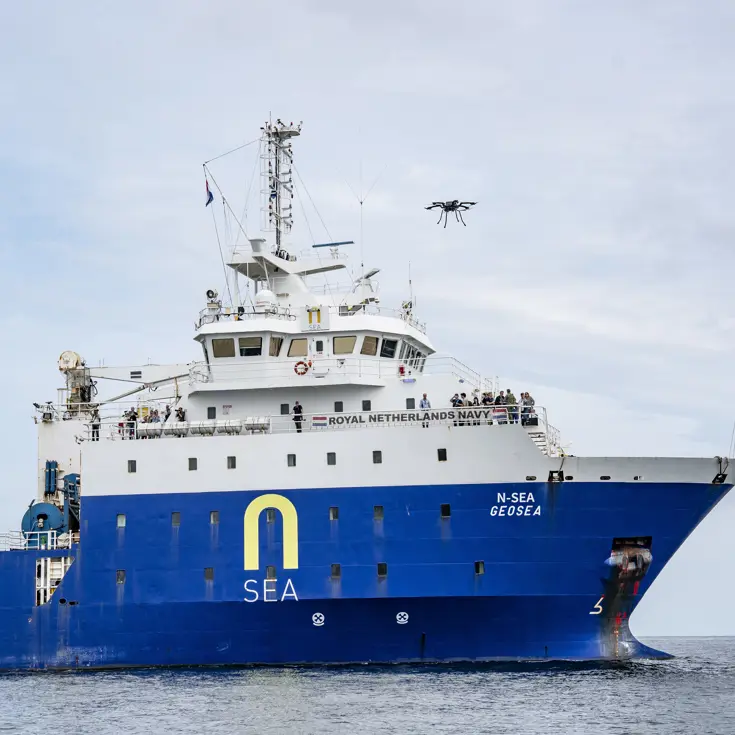 Een drone vliegt boven een groot, blauw schip op zee.
