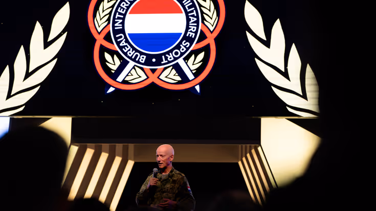 Brigadegeneraal Laurens Jobse achter een spreekgestoelte met een spandoek op de achtergrond.